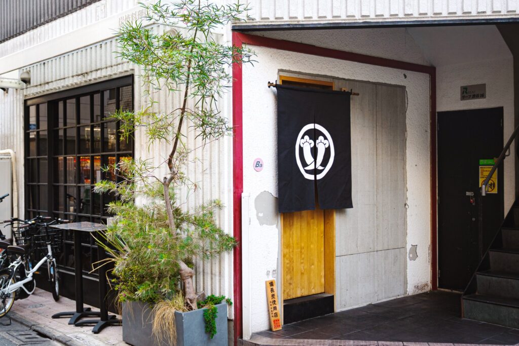 YAOYA Ba の外観。黒い暖簾と植栽のある白い建物